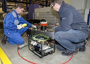 Zwei Personen knien und arbeiten an Industrieanlagen in einer Fabrik.