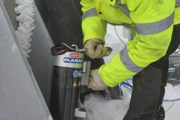 Anwendung_PSQ_0163 A worker in a yellow jacket skillfully operates machinery on a snow-covered, icy surface, demonstrating the performance and precision of the "Powerful Multi-Stage Tensioner from Plarad.