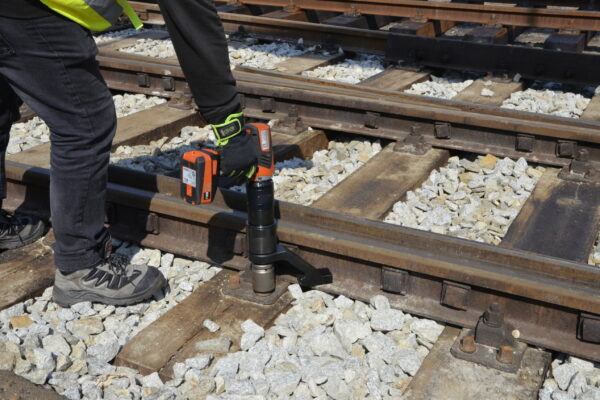 _DSC4964 A person expertly fasten the bolts of railway track with an DA2 battery torque gun from Plarad, showcasing an innovative transportation industry solution amidst the surrounding gravel.