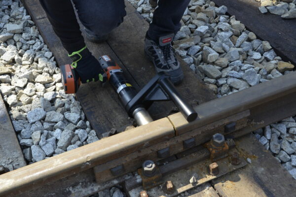 _DSC5011 A person uses a Plarad tool DA2 to tighten a bolt with a special reaction arm on a gravel-surrounded railway track, demonstrating the tool's efficiency as part of a transportation industry solution.