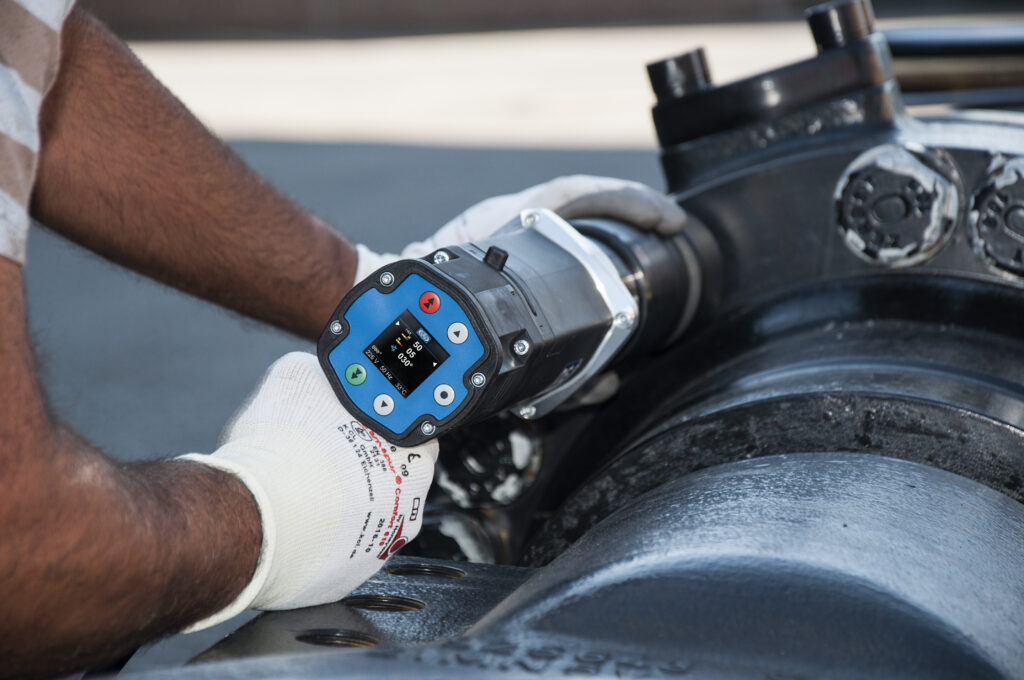Eine Person mit Handschuhen bedient einen digitalen Drehmomentschrauber an Industrieanlagen im Freien und demonstriert so die Präzision und Zuverlässigkeit von Schraubtechnik Made in Germany.