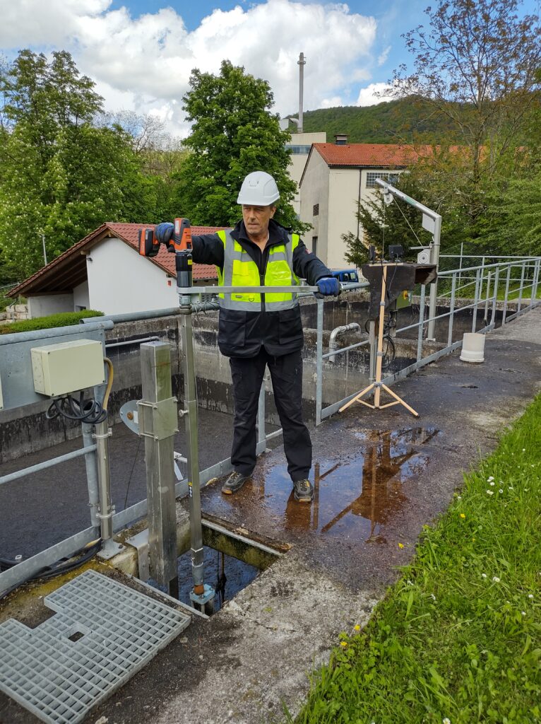 A worker in protective clothing expertly handles the equipment of a wastewater treatment plant outdoors on a partly cloudy day, using German-made bolting tools DA2 motion.
