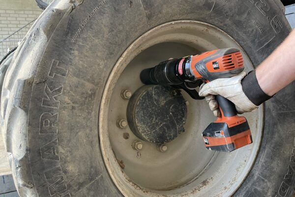 A person using a drill on a large tractor tire in a garage or workshop, a type commonly used for forestry equipment.