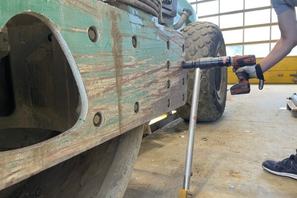A person using a nutrunner on a large tractor tire in a garage or workshop, a type commonly used for forestry equipment.