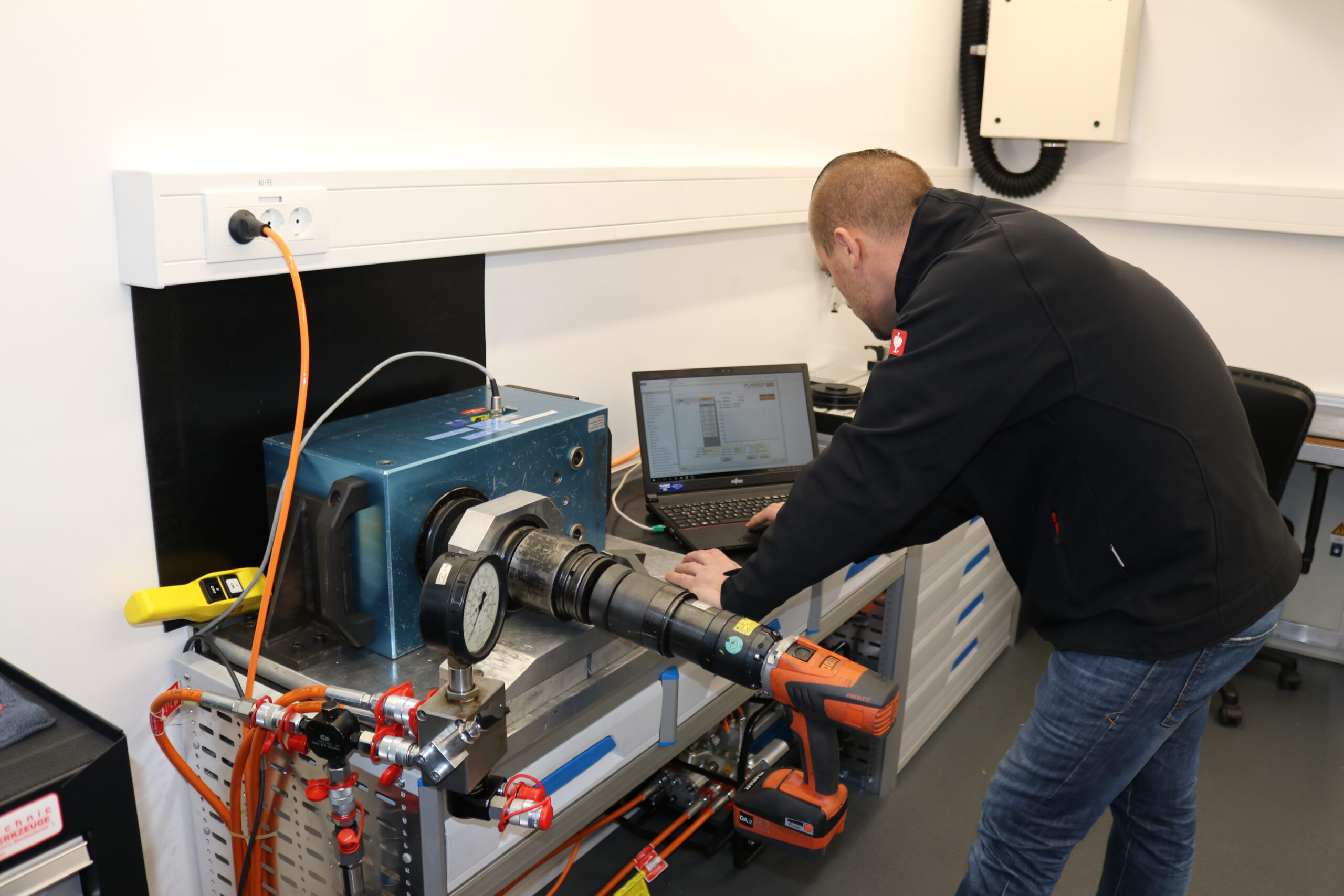 A person uses a laptop next to industrial equipment in a workshop, benefiting from Plarad's on-site customer service for expert assistance with their bolting challenges.