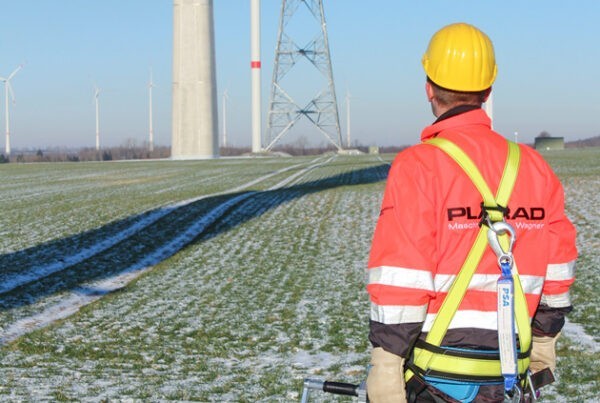Ein Arbeiter in Sicherheitsausrüstung und Helm steht auf einem schneebedeckten Feld und betrachtet eine im Bau befindliche Windkraftanlage. Er hält unseren Sicherheits-Nutrunner, der speziell für die Windindustrie in Zusammenarbeit mit Siemens Gamesa entwickelt wurde.