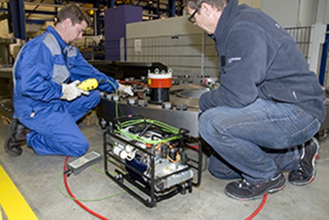 In the workshop, two technicians in protective gloves carefully work on industrial machines. They expertly handle the electrically powered TXE1docu unit from Plarad, ensuring precision and safety with every task.