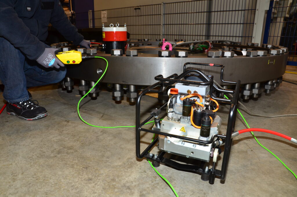 In an industrial environment, the technician skillfully operates a hydraulic bolt tensioner on a large metal structure, utilizing the precision of the fully automated XE1power unit for Plarad's bolting technology.