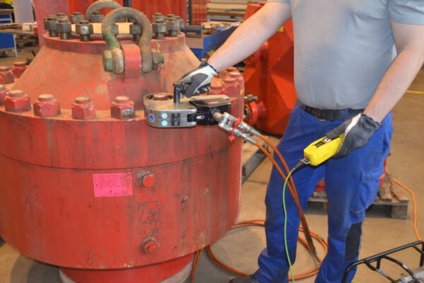 Eine Person verwendet fachmännisch einen hydraulischen Drehmomentschlüssel FSX an einem großen roten Industriegerät in einer Werkstatt und demonstriert Schraubsysteme für energieerzeugende Industrien.