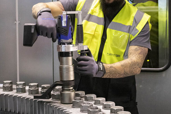A person uses a power tool to tighten bolts on industrial equipment, demonstrating the precision and reliability of the "Made in Germany" DA2 Safety battery nutrunner.