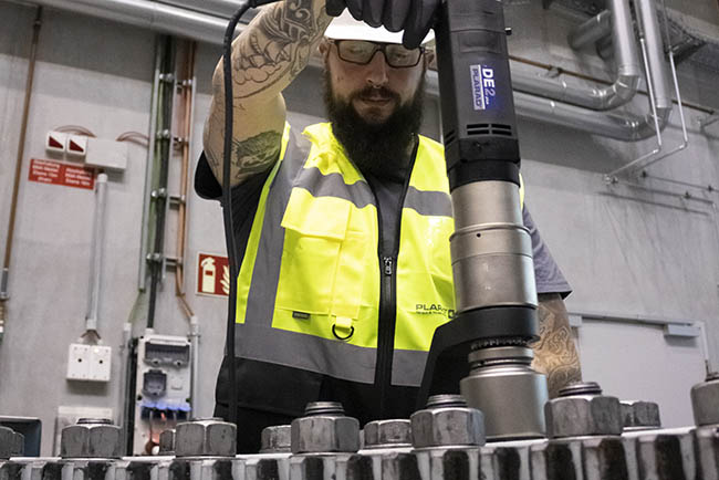In an industrial facility, a worker in a high-visibility vest expertly operates a "Made in Germany" DE 1 nutrunner while working on metal parts.
