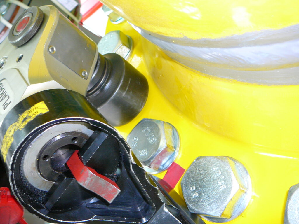 P1050170 Close-up of an industrial machine featuring a yellow component, large bolts, and a black-red lever, with the Plarad MXEC hydraulic torque wrench, one of the top-selling models, in operation.