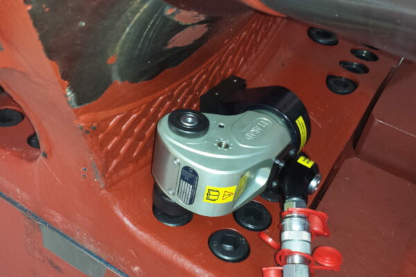 A hydraulic square drive wrench from Plarad is expertly used on a metal structure, featuring visible bolt connections highlighted by a vibrant red coating.