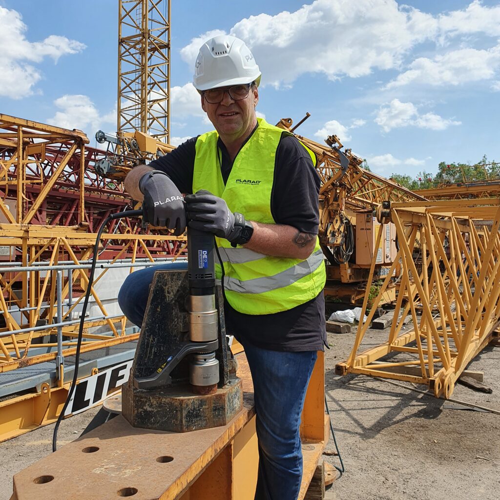 Under a sunny sky, a worker in protective gear expertly operates the Plarad DE1power, a modern electric nutrunner, ensuring precision and efficiency on the construction site.