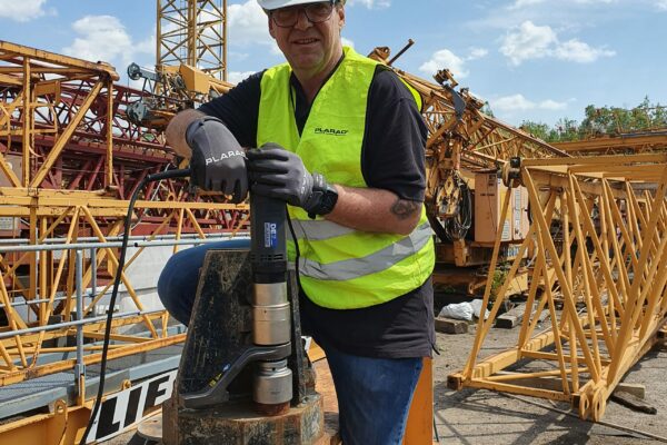 Under a sunny sky, a worker in protective gear expertly operates the Plarad DE1power, a modern electric nutrunner, ensuring precision and efficiency on the construction site.