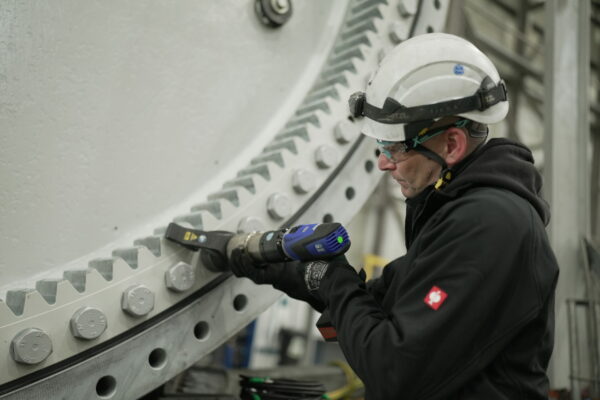 A worker in protective gear expertly uses a power tool on a large industrial machine with bolts, demonstrating the precision of the battery-powered torque wrench and bolting technology from PLARAD.