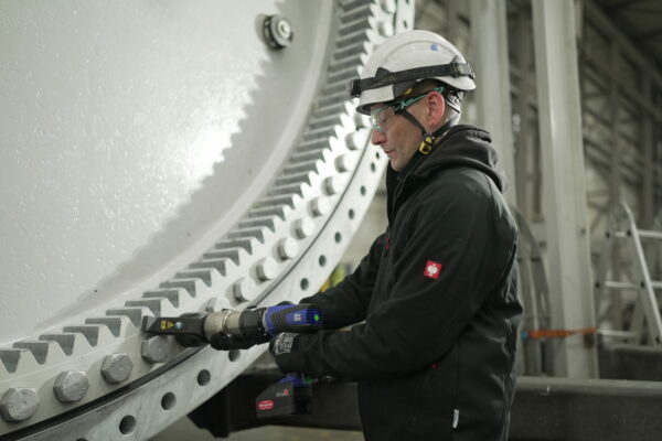 A worker in protective gear expertly uses a DA2 nutrunner on the hub of a wind turbine, demonstrating the precision of the battery-powered torque wrench and screw technology from PLARAD 🔧.