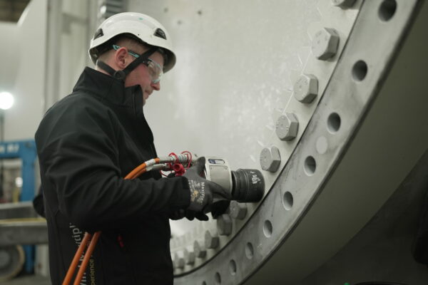 A worker carefully tightens bolts on the hub of a wind turbine using a hydraulic square drive wrench from Plarad, wearing the necessary safety gear.