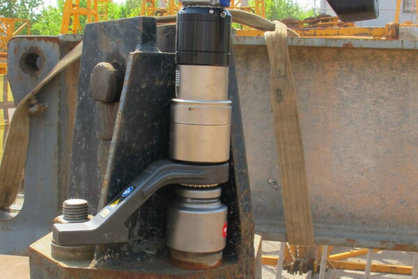 A torque wrench tightens a large bolt on a segment of a crane, with cranes rising in the background. Nearby, a battery-powered torque wrench.