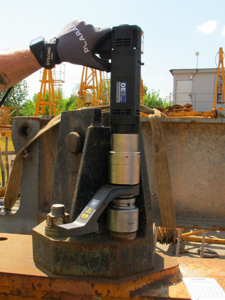 A person expertly operates the Plarad DE1power, an advanced electric nutrunner, on a large industrial bolt on a busy construction site, demonstrating precision screwing technique.
