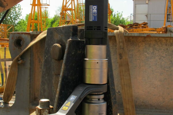 A person expertly operates the Plarad DE1power, an advanced electric nutrunner, on a large industrial bolt on a busy construction site, demonstrating precision screwing technique.