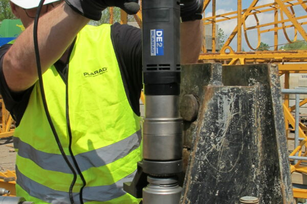 A worker wearing a safety vest and helmet expertly applies the Plarad DE1power electric nutrunner to construction machinery outdoors, ensuring precision and efficiency.