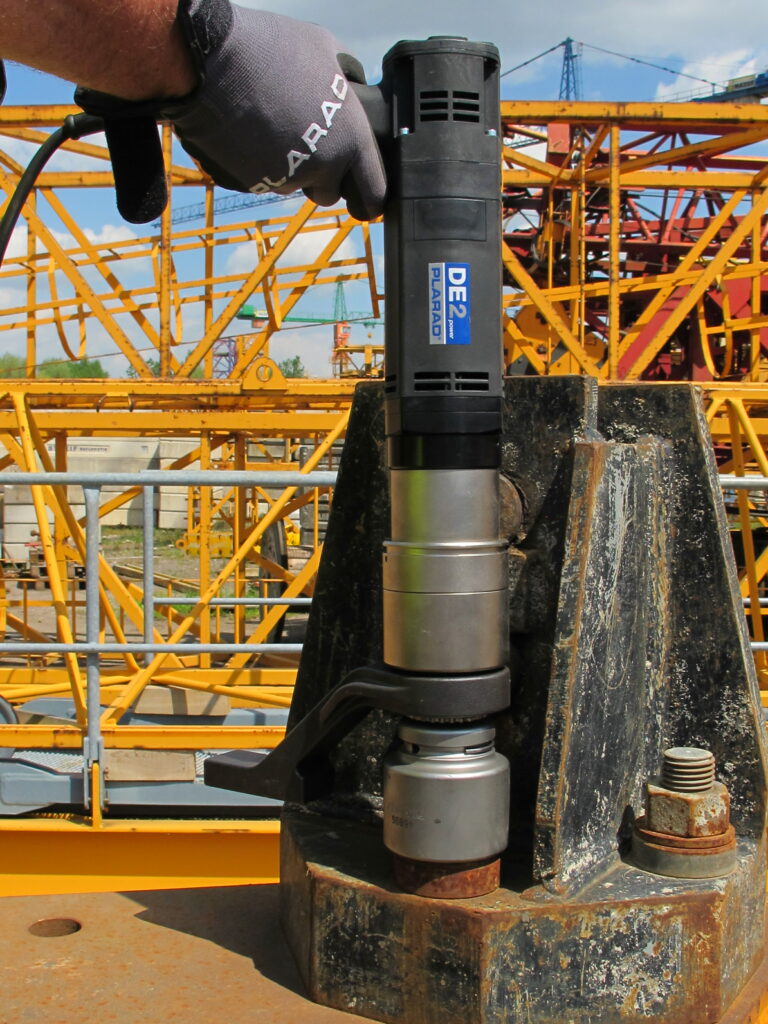 A person skillfully applies the Plarad DE1power to a large bolt, with bright yellow construction machinery in the background.