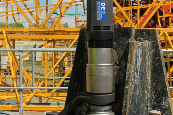 A person skillfully applies the Plarad DE1power to a large bolt, with bright yellow construction machinery in the background.