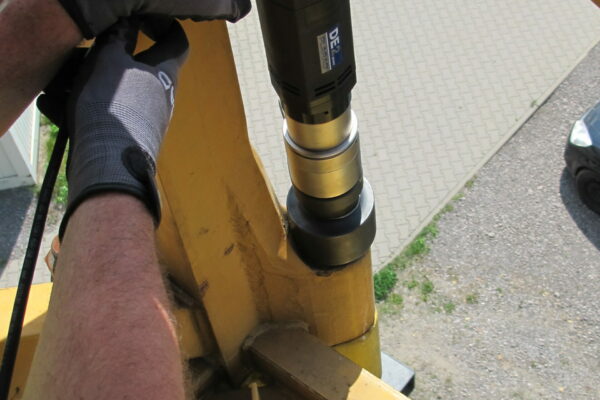 The person skillfully operates machinery on a metal structure, wearing gloves and a helmet. They precisely use the Plarad DE2power electric nutrunner while positioned above a paved surface below.