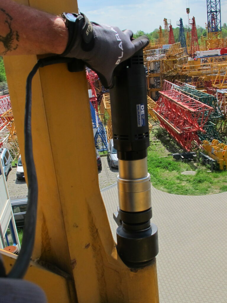 A worker uses the DE1power from Plarad, a modern electric nutrunner, to fasten a bolt to a yellow steel beam on the construction site.