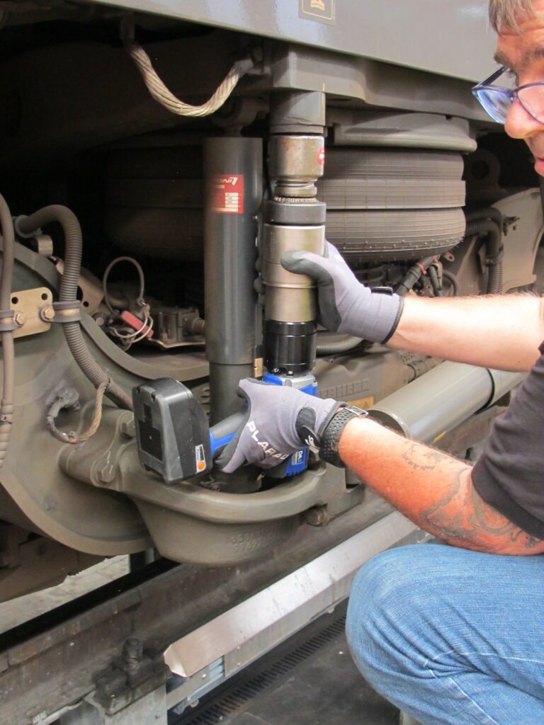 IMG_2051 A person expertly works with a DA2 battery-powered torque wrench on the train suspension, wearing gloves and safety glasses for protection.