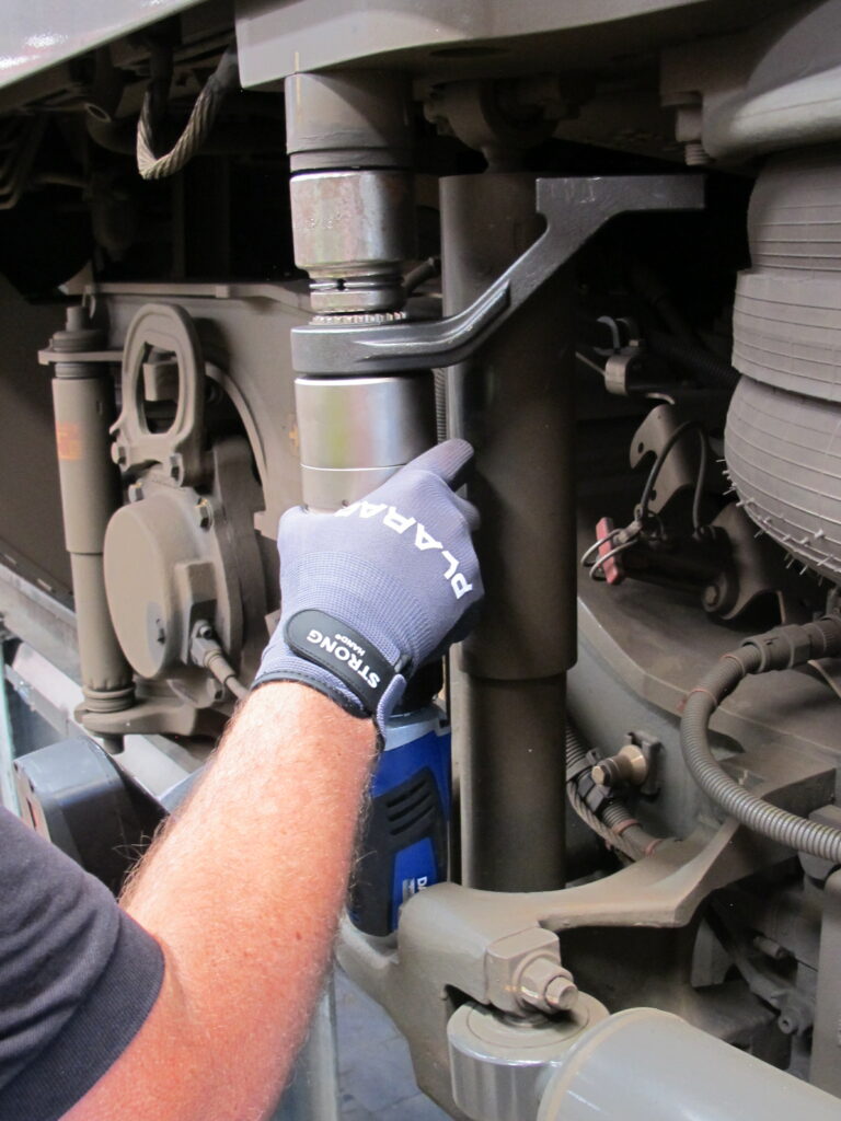 IMG_2054 A person with blue gloves expertly adjusts the suspension system of a train using a battery-powered torque wrench on train engine.