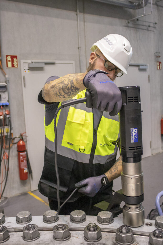 In a facility, a worker in protective gear expertly uses the Plarad DE1power electric nutrunner on industrial equipment.