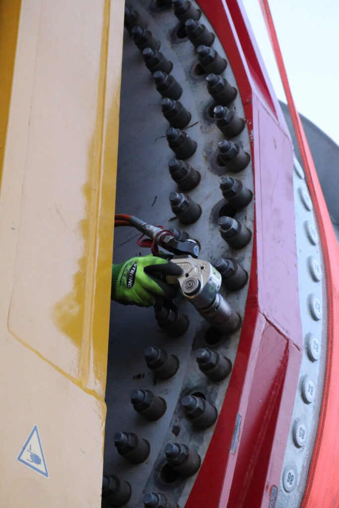 IMG_3599 A person wearing green gloves operates a hydraulic square drive wrench from Plarad on large bolts in industrial machinery.