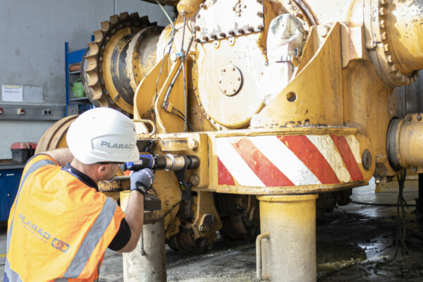 A worker in protective gear meticulously inspects CAT Bulldozer in a workshop, using the precision of the battery-powered torque wrench and bolting technology from PLARAD to ensure smooth operation.