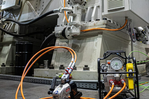 Ein Hydraulikwerkzeug und eine Pumpeinheit von Plarad, angeschlossen an eine große Industriemaschine in einer Werkshalle