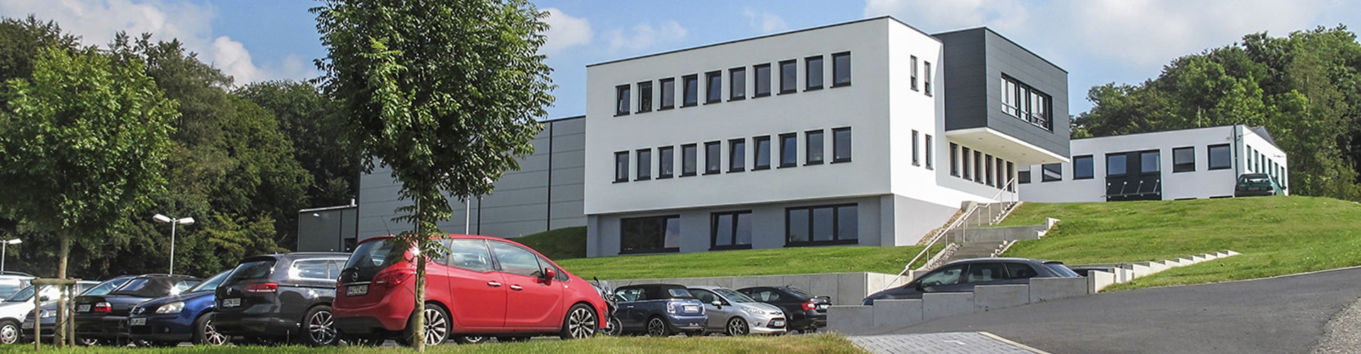 Modernes Bürogebäude mit großen Fenstern, umgeben von geparkten Autos