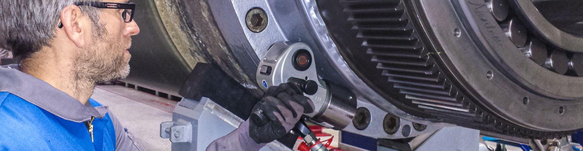 Arbeiter mit hydraulischen Schrauber an einer großen Maschine