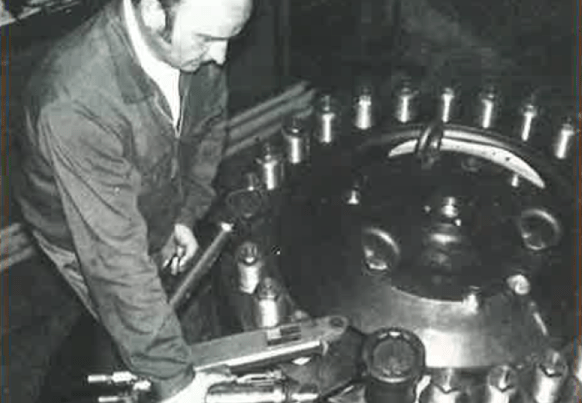 In a workshop setting, a man skillfully operates heavy industrial machinery with a large wrench.