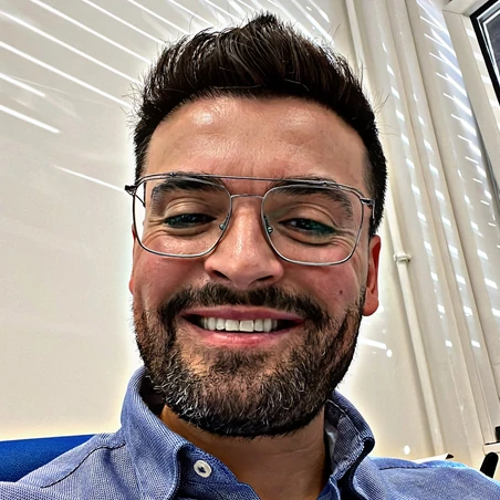 A man with glasses and a beard, smiling confidently at the camera indoors, embodies the reliability of Plarads 24/7 global service network.