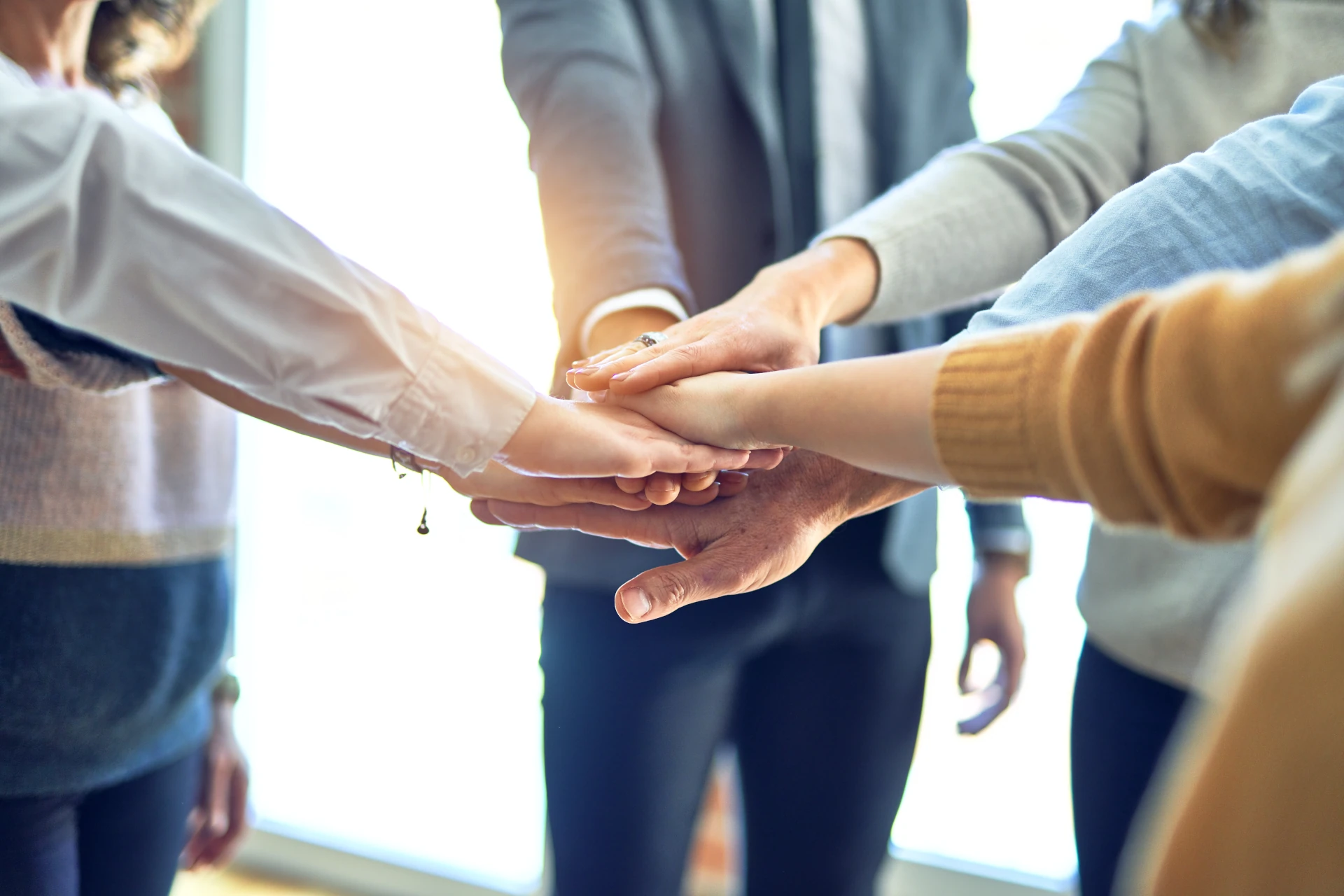 A group of people stacking their hands together, symbolizing teamwork and unity, as they explore aktuelle Stellenangebote to find a promising career with Plarad.